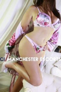 Close up of Geri stood up against a white background wearing pink and purple flowery lingerie and heels